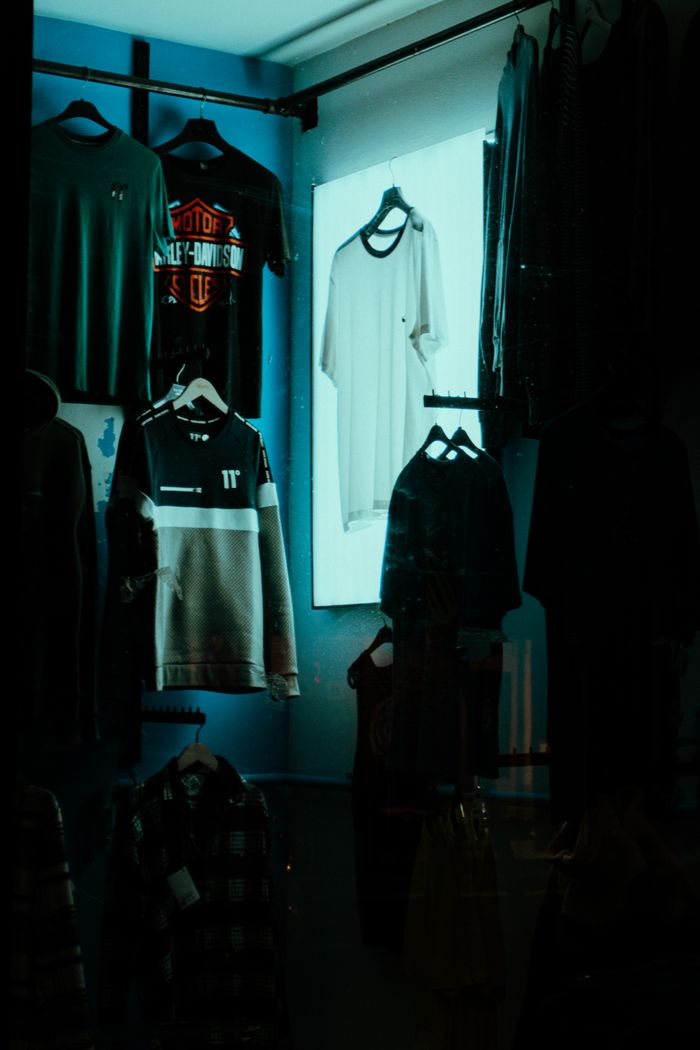 Dark and stylish display of hanging clothes in a retail store window.