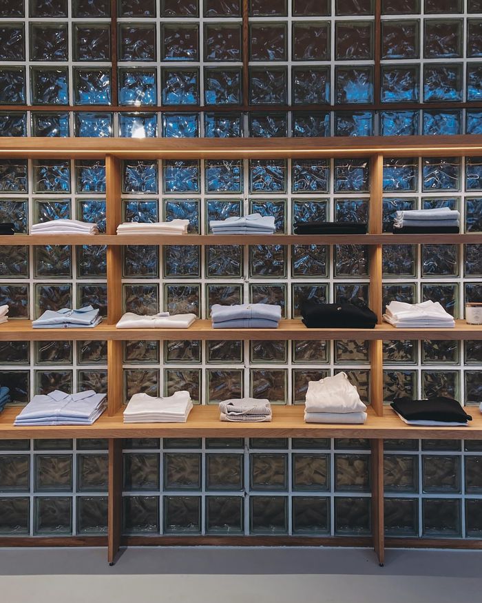 Organized display of folded shirts on wooden shelves against a glass block wall.